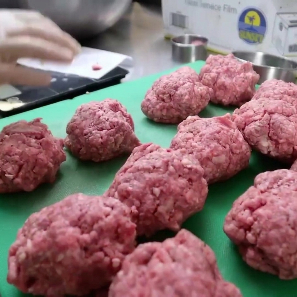 Carne de bisonte molida siendo empacada en un molde circular para formar hamburguesas gruesas.