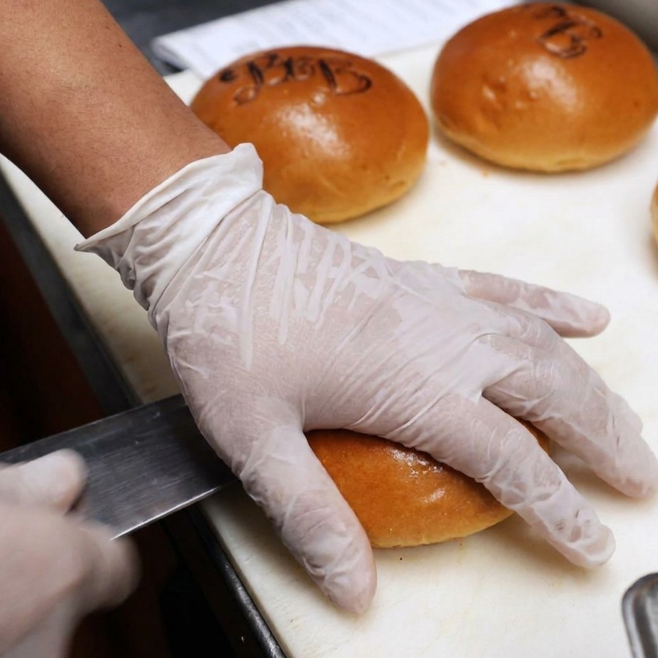 Panes de hamburguesa siendo cortados y cubiertos con mantequilla para la plancha.