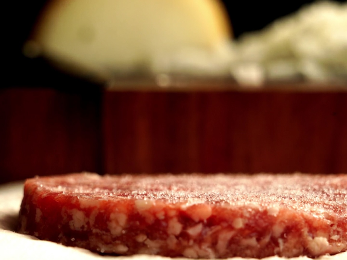 Primer plano de una hamburguesa de ternera Wagyu siendo sazonada con pimienta negra recién molida.