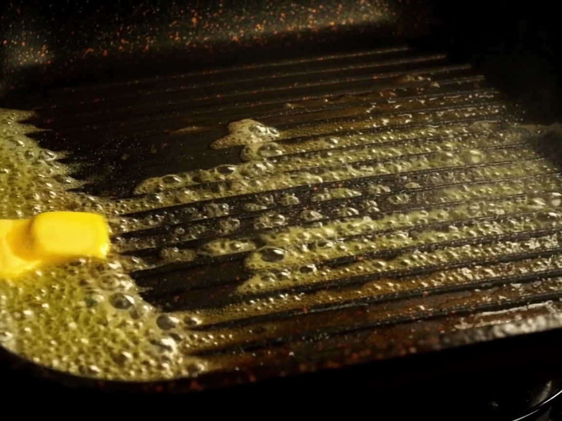 Mitades de pan de hamburguesa tostándose en una sartén grill con mantequilla derretida.