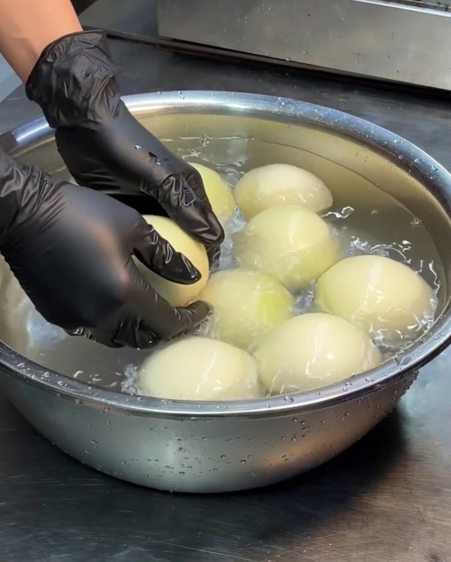 Cebollas blancas enteras en un recipiente de acero inoxidable con agua.