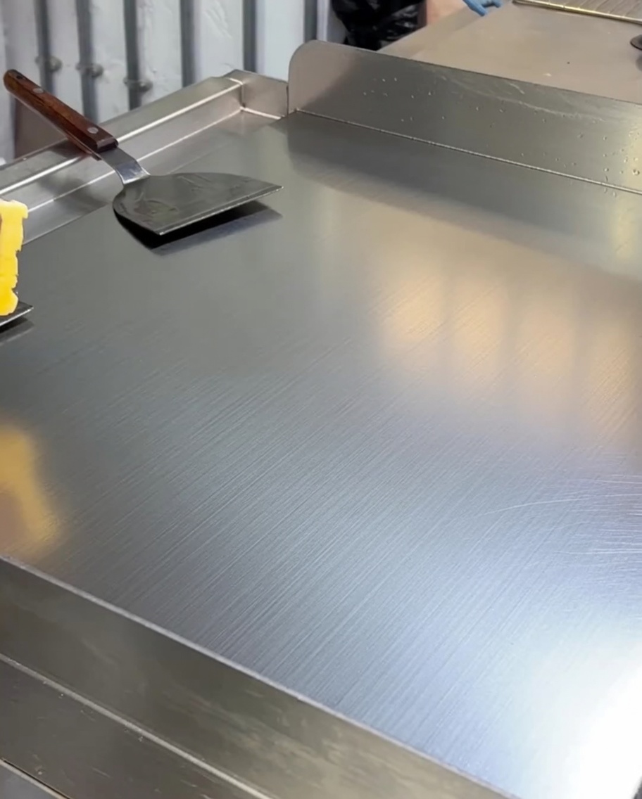 Mantequilla amarilla derritiéndose y cubriendo la superficie de una plancha caliente.
