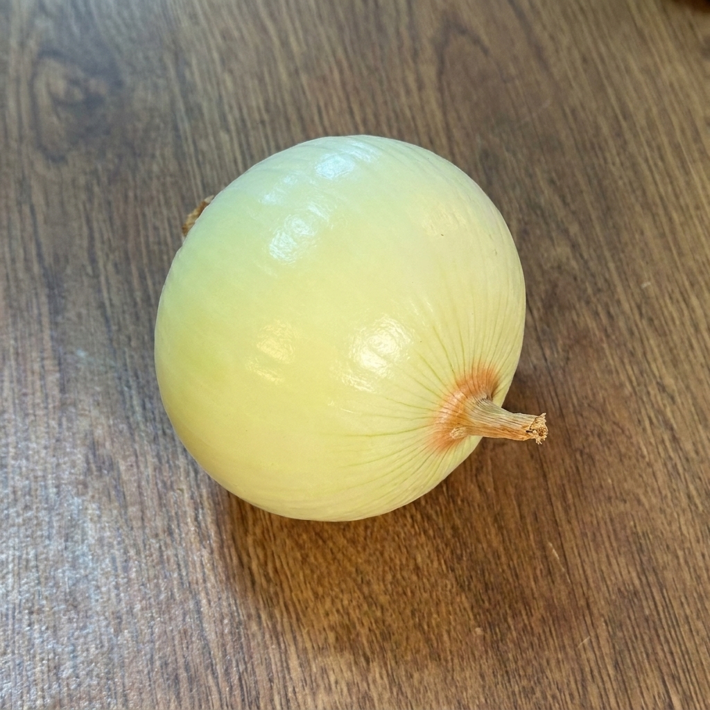 Una cebolla entera pelada reposando sobre una superficie de madera.