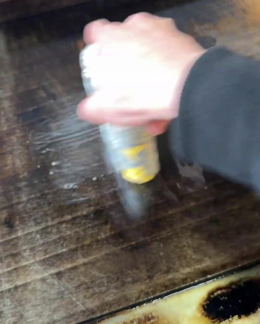 Una mano untando mantequilla derretida sobre la superficie de una plancha caliente.