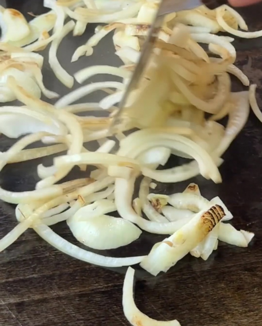 Cebollas removidas en la plancha con una espátula mientras empiezan a ablandarse y cocinarse.
