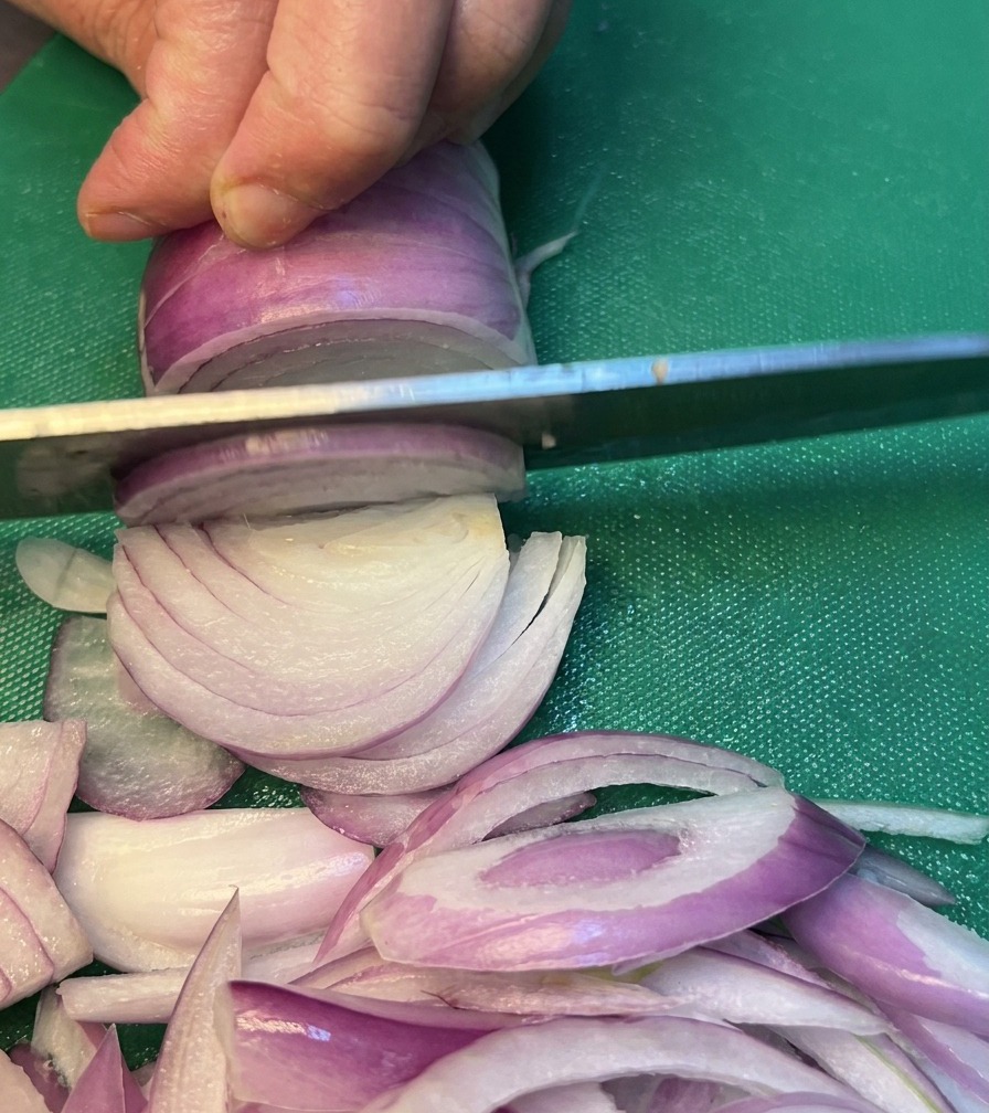 Cebollas siendo cortadas cuidadosamente en una tabla de cortar verde.