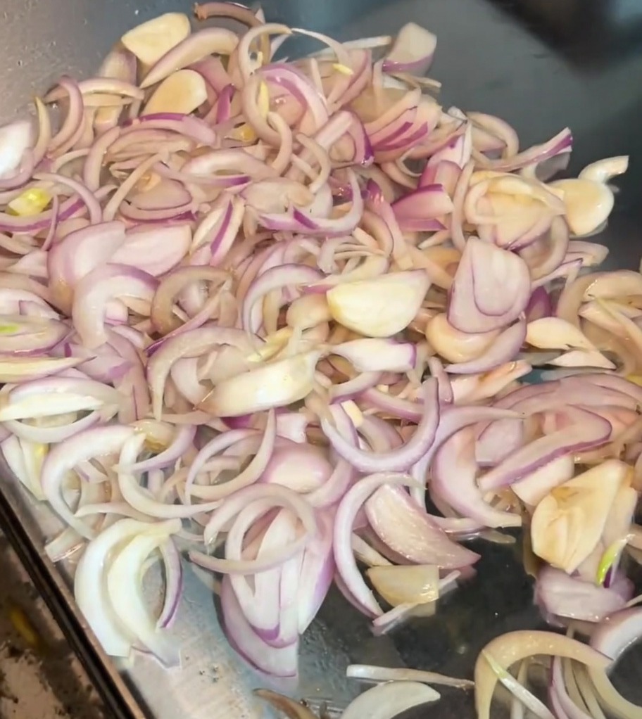 Rodajas de cebolla removiéndose en una plancha caliente con una espátula de metal.