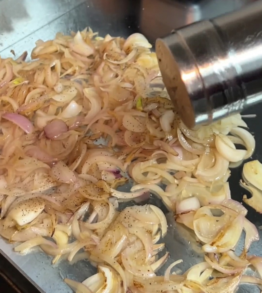 Sal y pimienta negra espolvoreándose sobre las cebollas salteadas en la sartén.