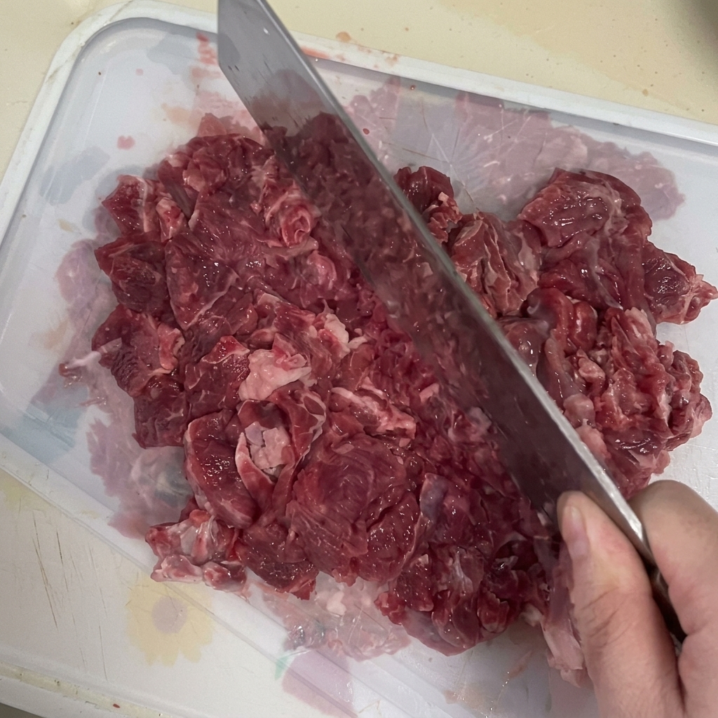 Un cuchillo de carnicero siendo utilizado para picar carne de res fresca sobre una tabla.