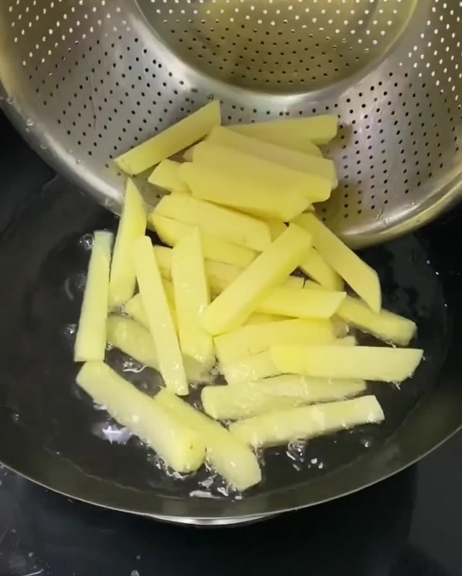 Tiras de patata hirviendo en un colador sumergido en una olla de agua caliente.