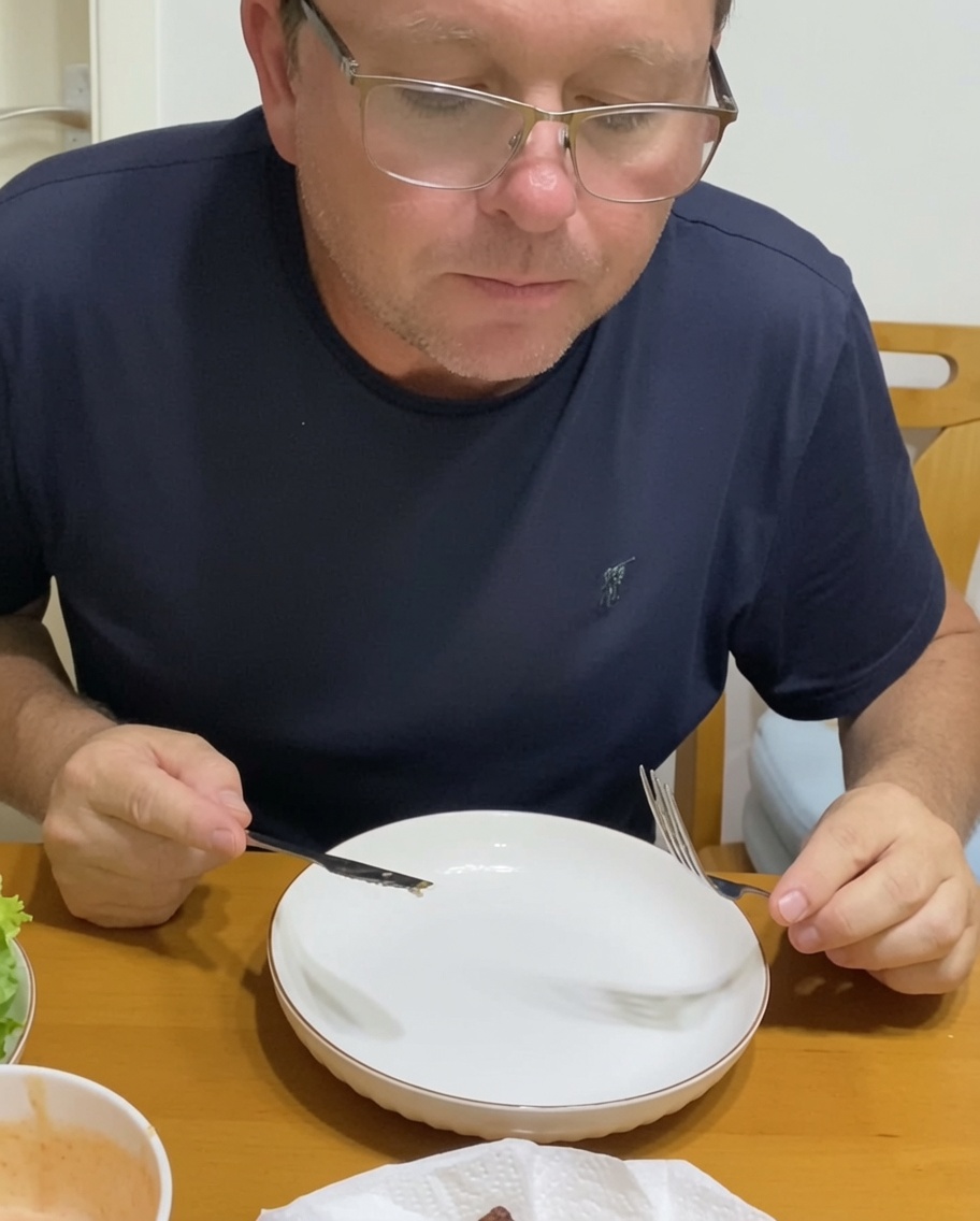 Persona montando una hamburguesa en un plato, añadiendo cebollas caramelizadas y verduras frescas sobre la carne en el pan.