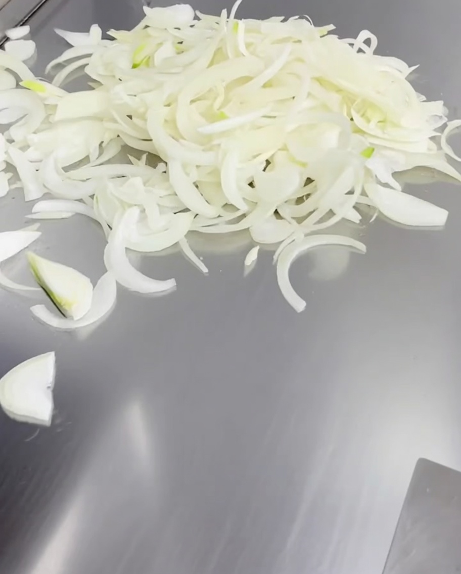 Tiras de cebolla blanca extendidas sobre la superficie de una plancha de metal caliente.