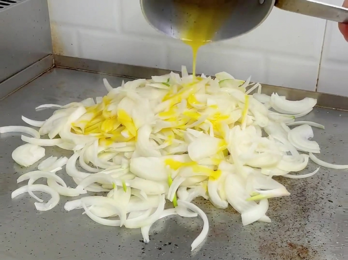 Cebollas siendo salteadas en una plancha caliente, luciendo suavizadas y ligeramente doradas.