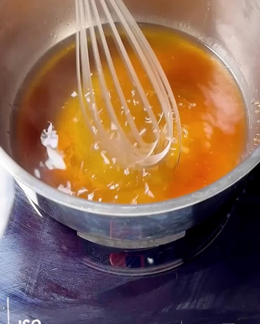 Batidor mezclando mermelada de cereza, bourbon y azúcar morena en una cacerola al fuego.