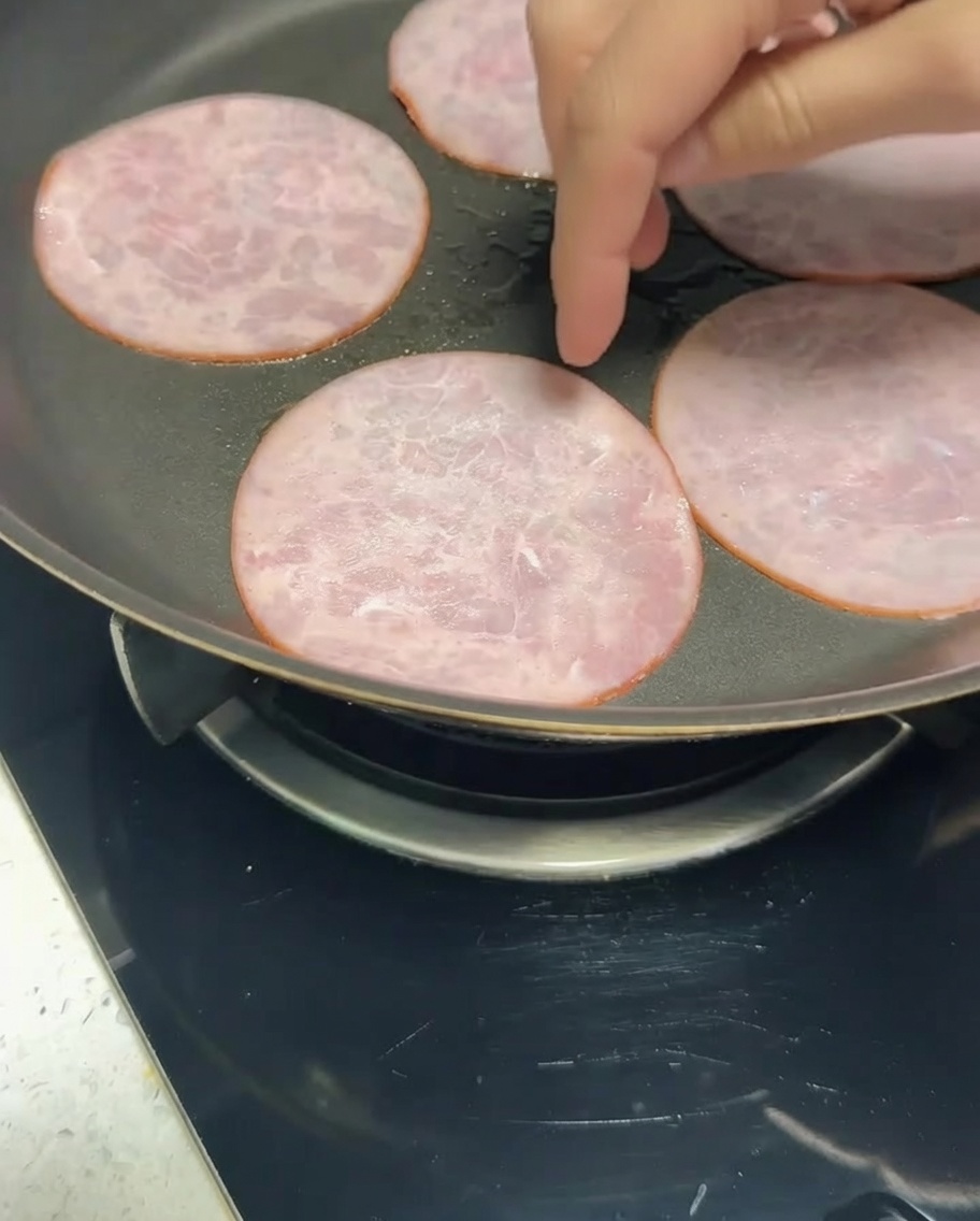 Tiras de bacon bajo en grasa friéndose en una sartén hasta dorarse.