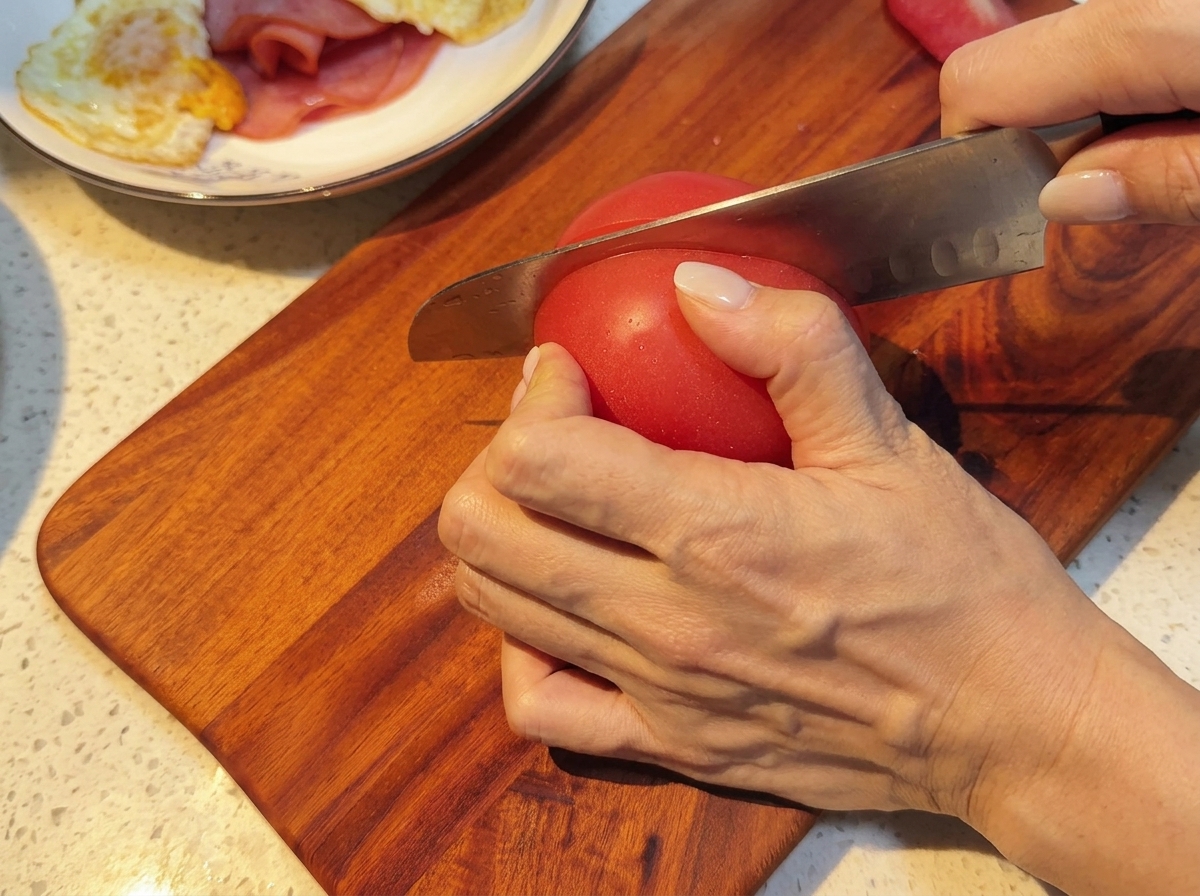 Tomates frescos siendo cortados en rodajas uniformes sobre una tabla de madera.