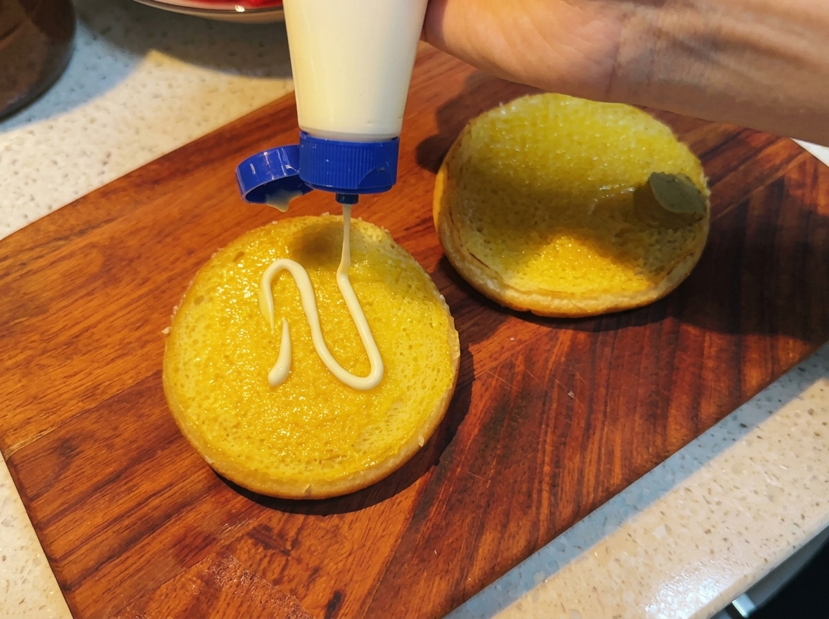 Mayonesa siendo añadida sobre el pan que ya tiene la mostaza.