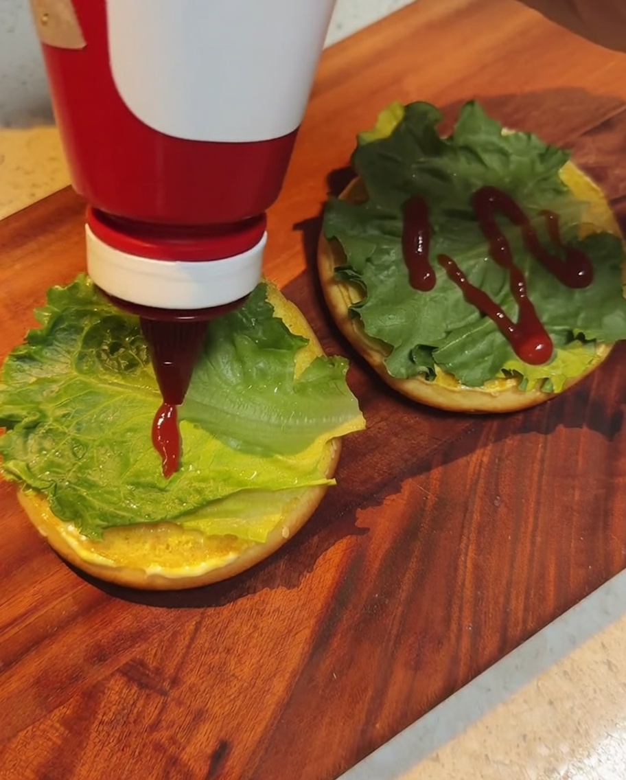 Kétchup rojo siendo vertido sobre las hojas de lechuga en el pan.