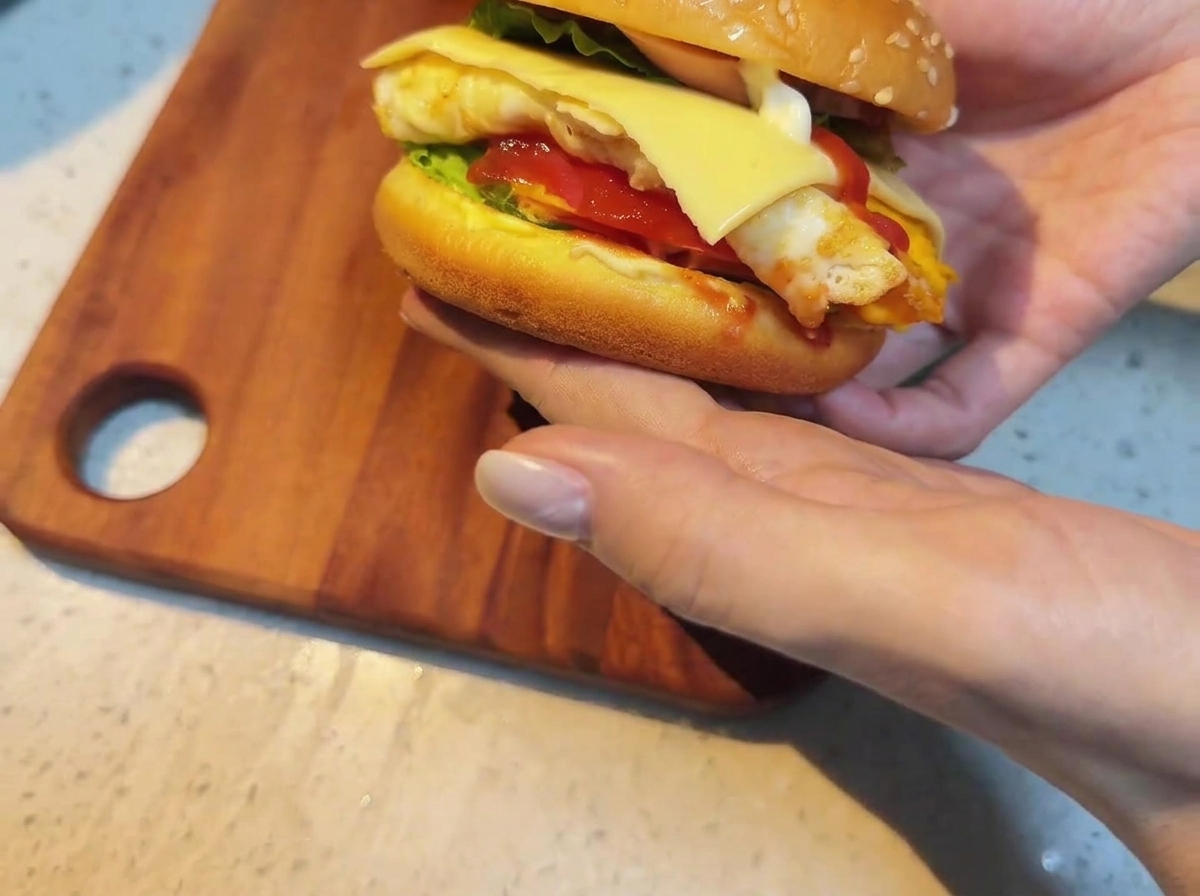 Una loncha de queso siendo colocada sobre la hamburguesa montada.