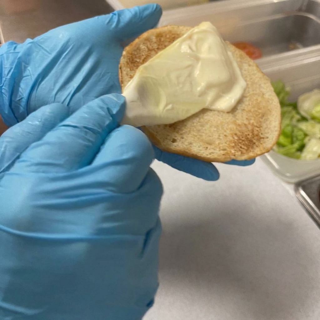 Un esparcidor de plástico aplicando una capa de mayonesa cremosa sobre la superficie tostada del pan.