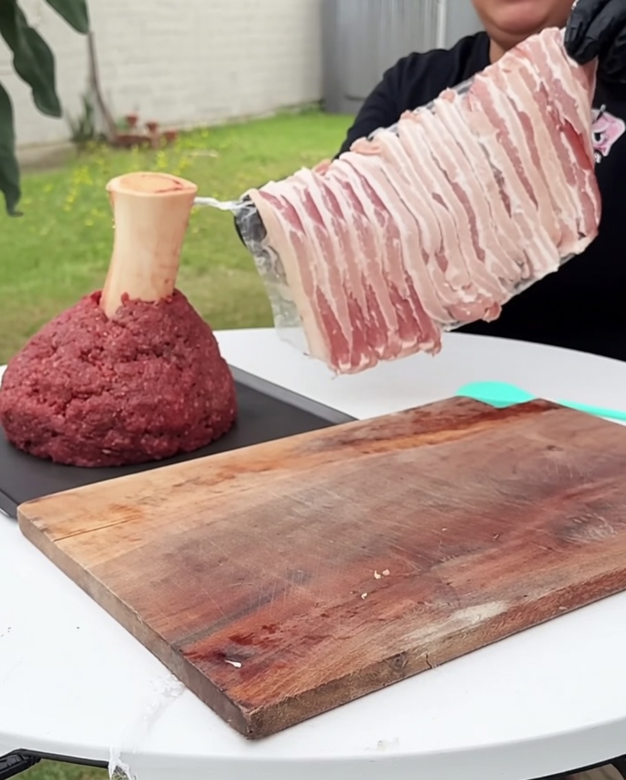 Bloque de carne molida envuelto cuidadosamente con tiras de tocino crudo en todos sus lados.