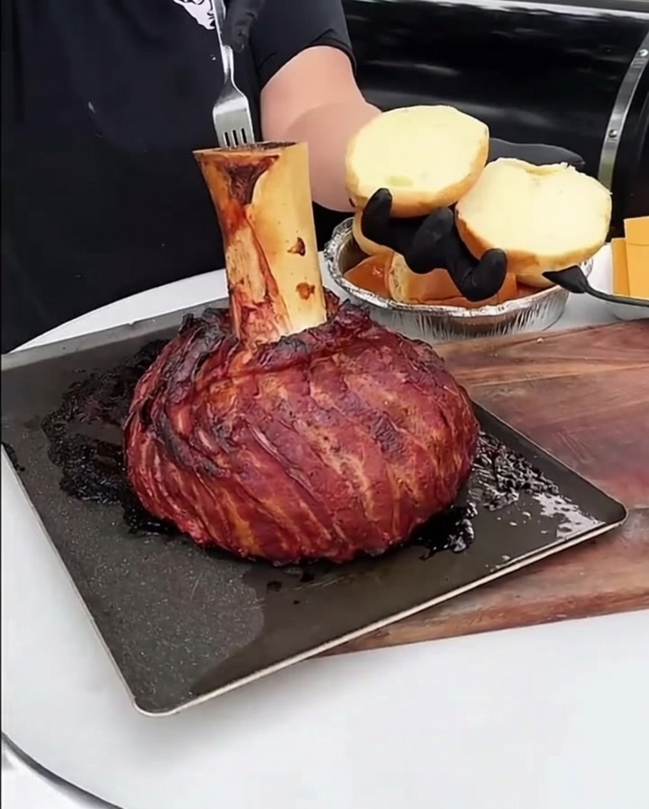 Cucharada de tuétano rico y asado siendo untada sobre la superficie de un pan de hamburguesa tostado.