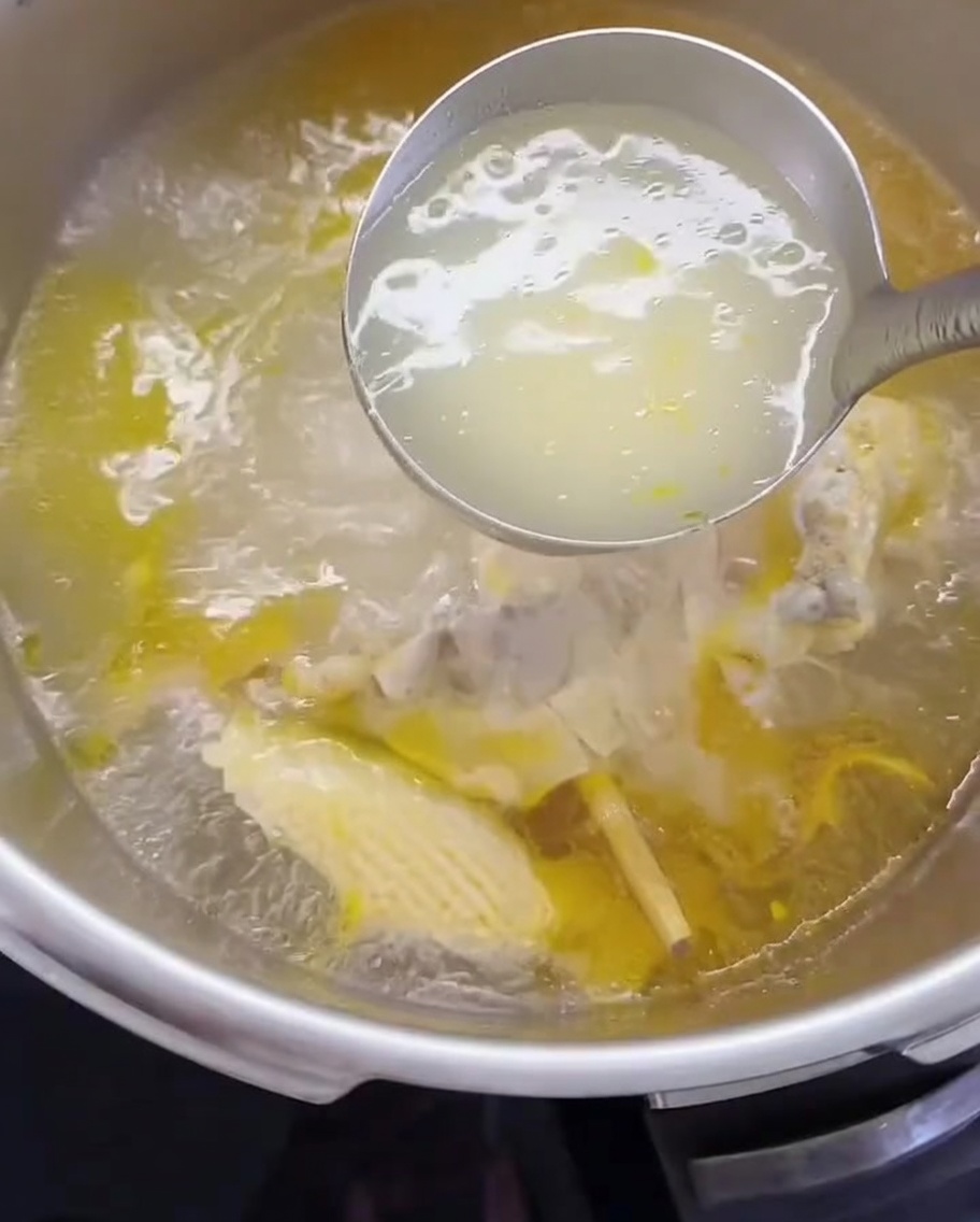 Un cucharón transfiriendo caldo de pollo y carne deshebrada a una olla.