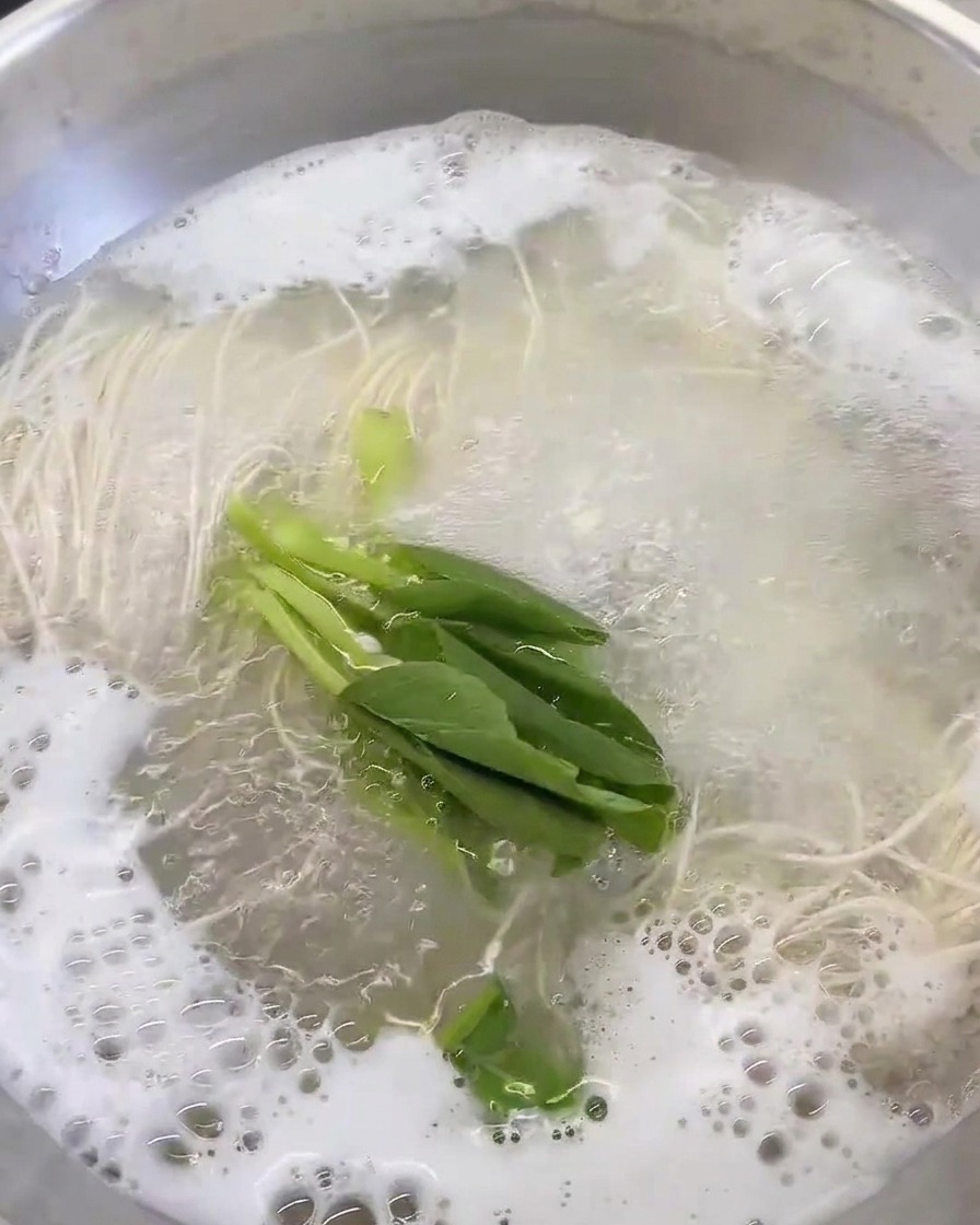 Verduras de hoja verde añadidas a la olla con caldo y fideos.
