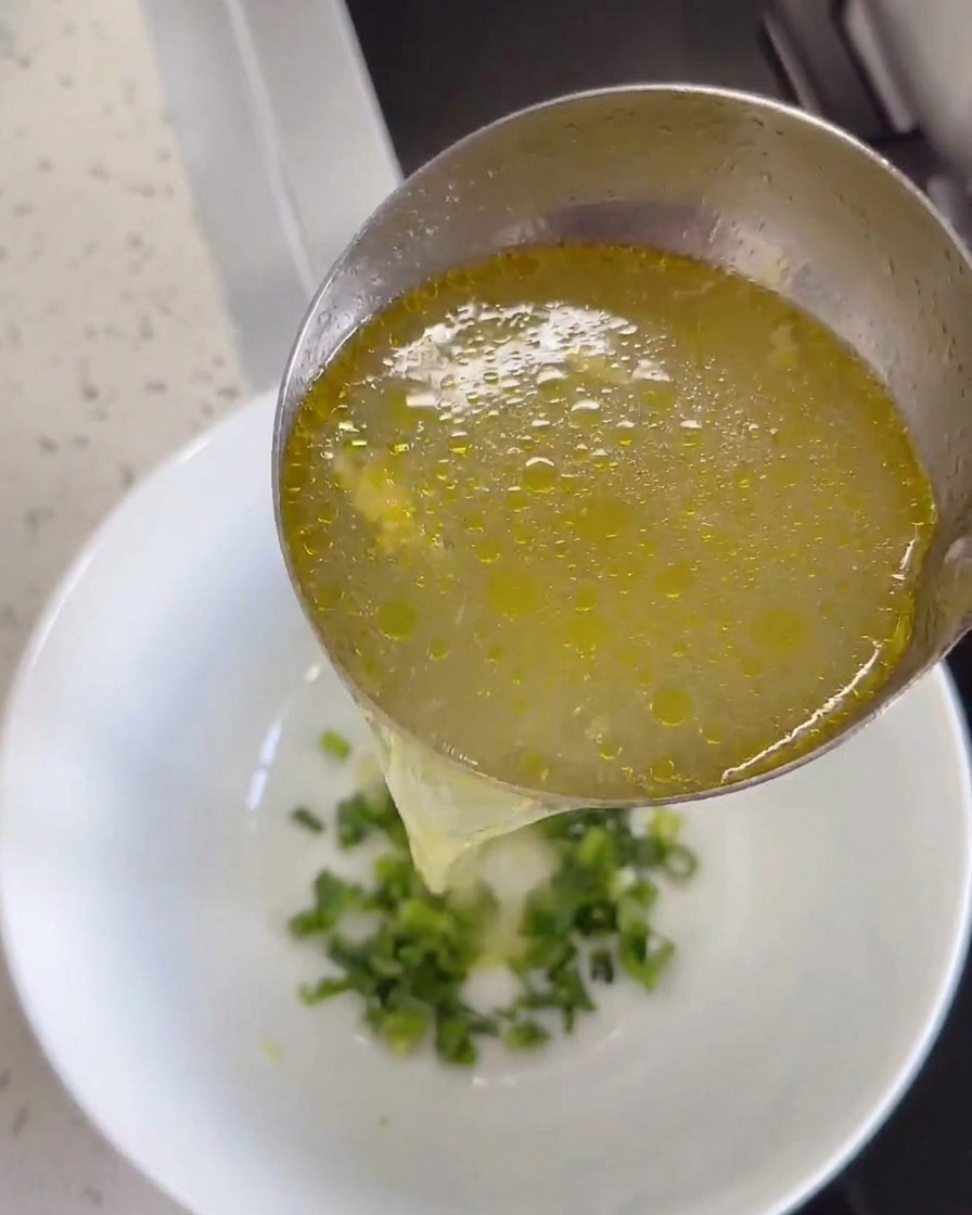 Caldo de pollo caliente vertido sobre un tazón con jengibre y cilantro.