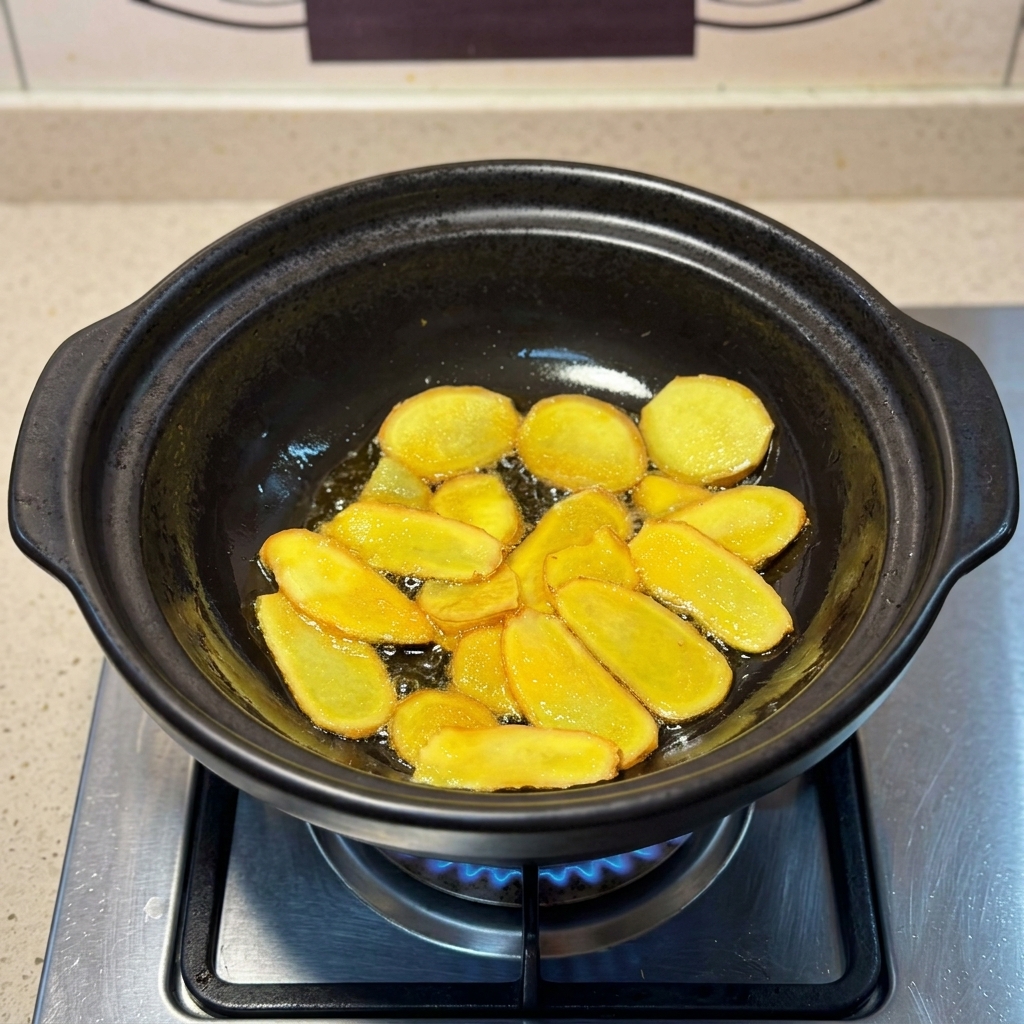 Láminas de jengibre doradas friéndose en aceite de sésamo brillante dentro de una olla de barro.