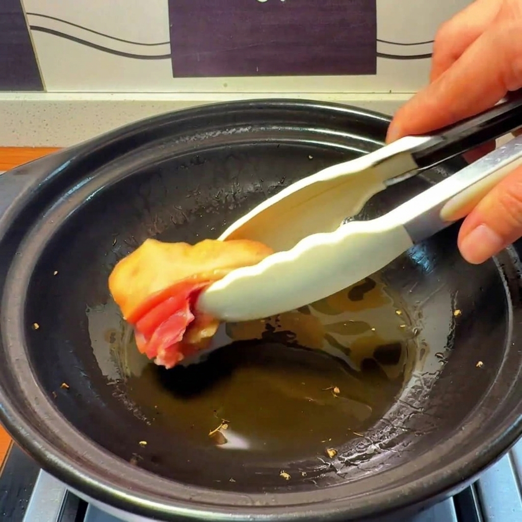 Trozos de pollo crudo colocándose en una olla de barro con aceite caliente infusionado con jengibre.