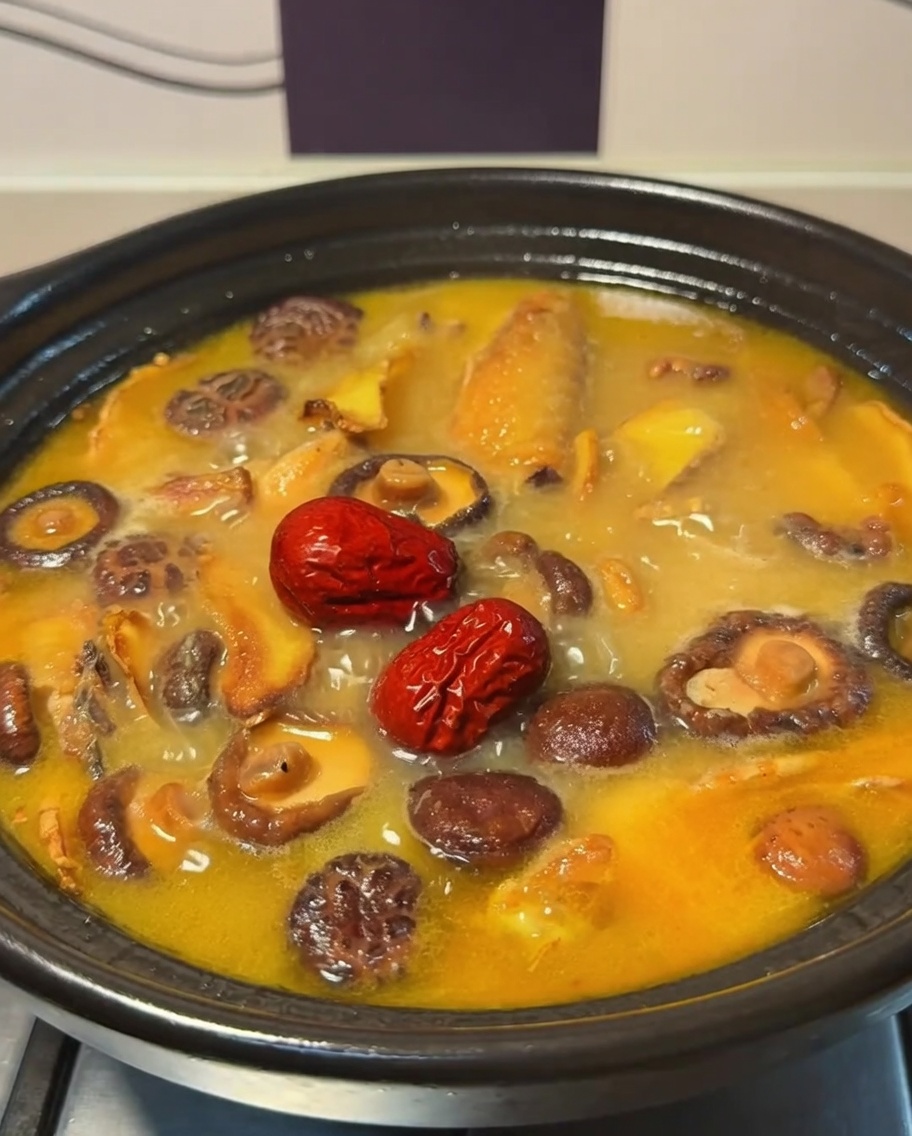 Dátiles rojos flotando en el burbujeante caldo de pollo y setas dentro de una olla de barro.