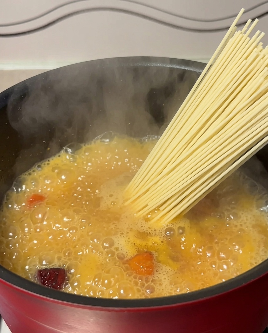 Fideos secos colocándose en una olla con sopa de pollo hirviendo.