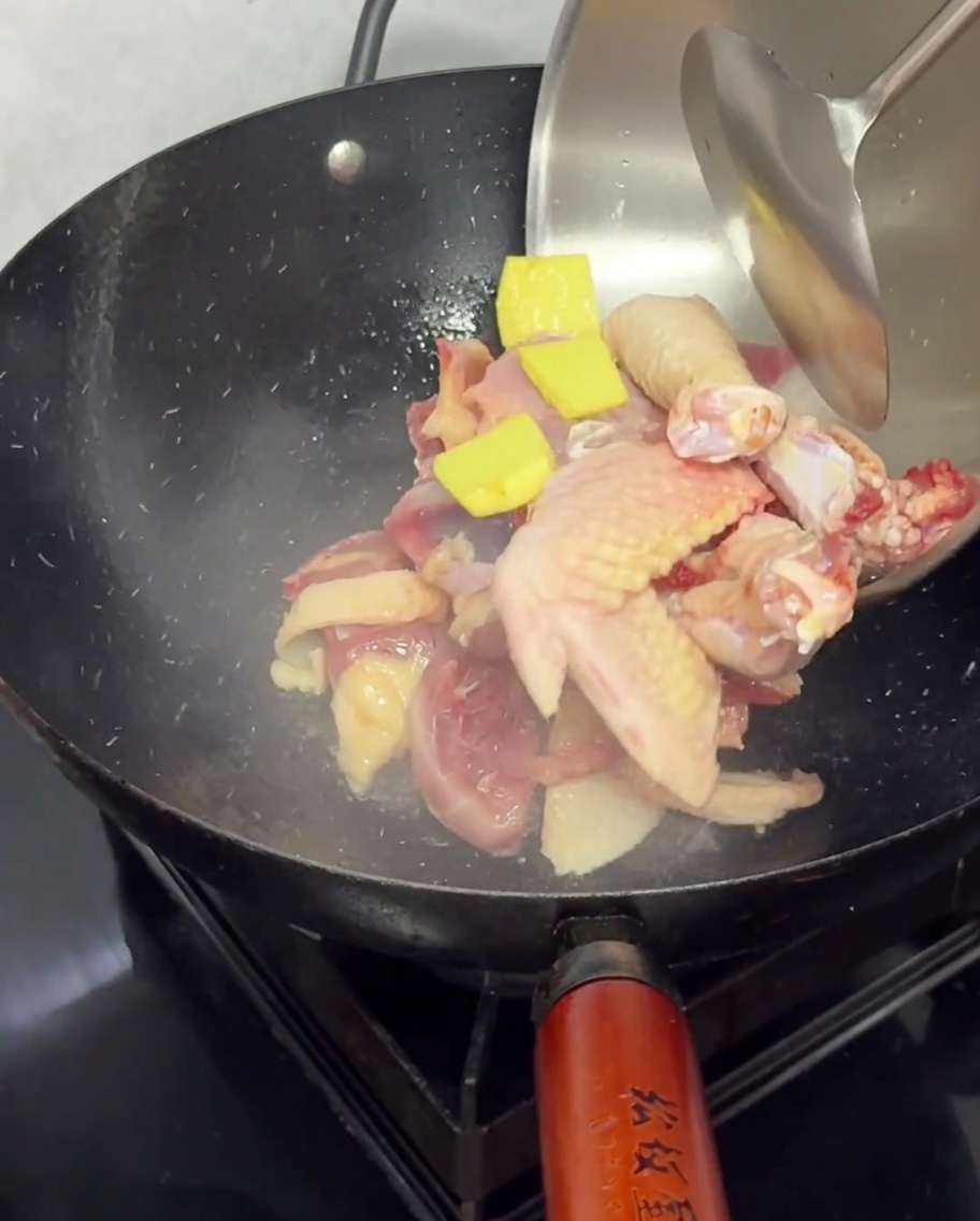 Piezas de pollo y rodajas de jengibre sofriéndose en un wok caliente.