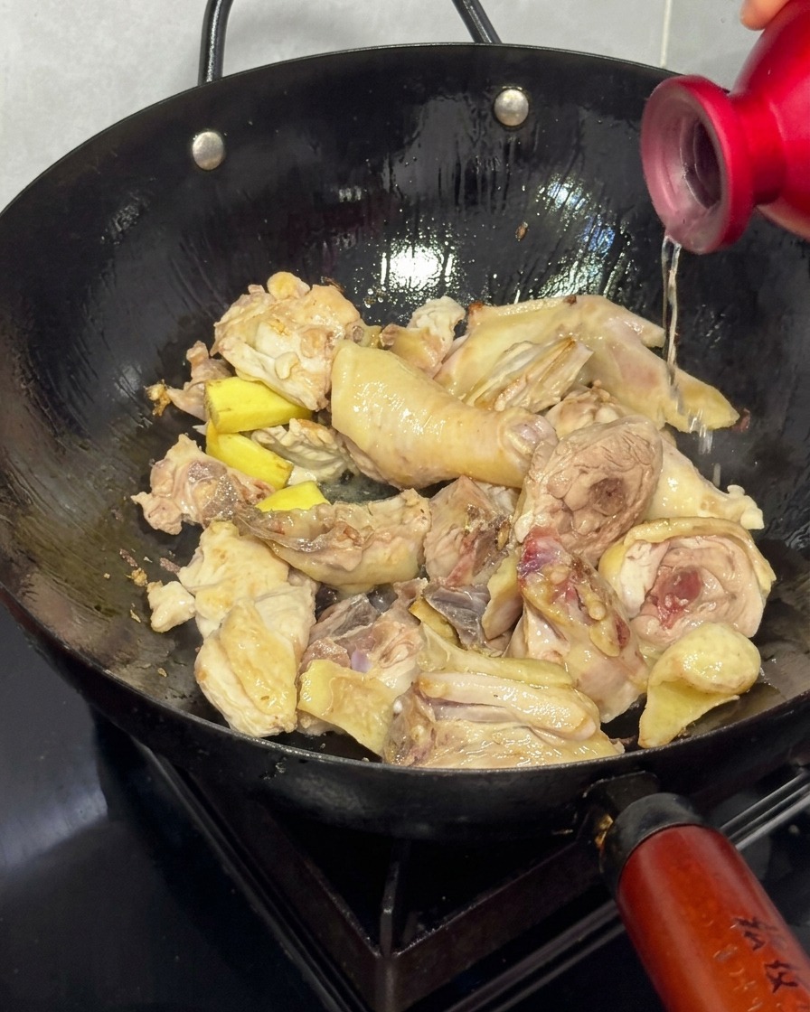 Vertiendo vino de arroz en un wok con pollo dorado y jengibre.