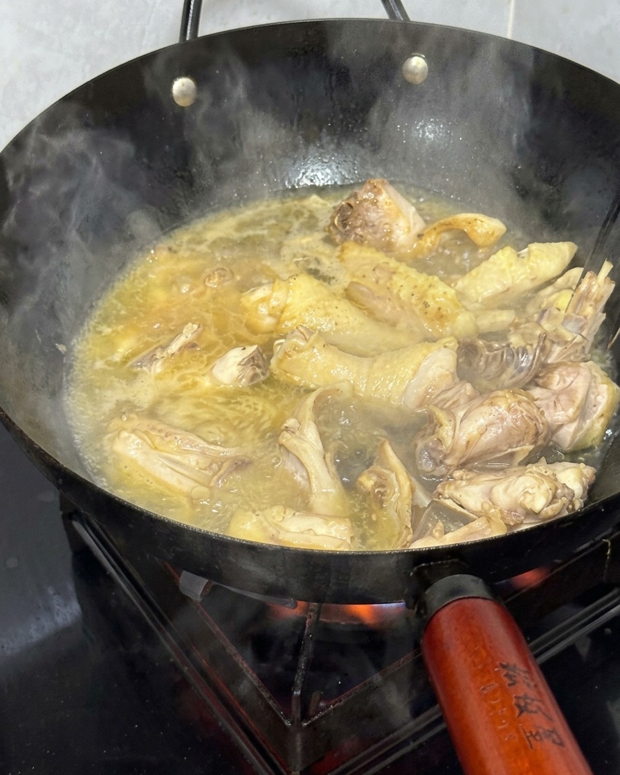 Piezas de pollo hirviendo en un caldo dorado dentro de un wok.