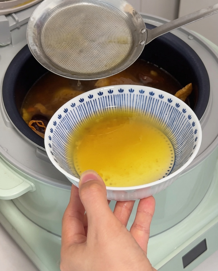 Un cazo retirando la grasa dorada de la superficie del caldo.