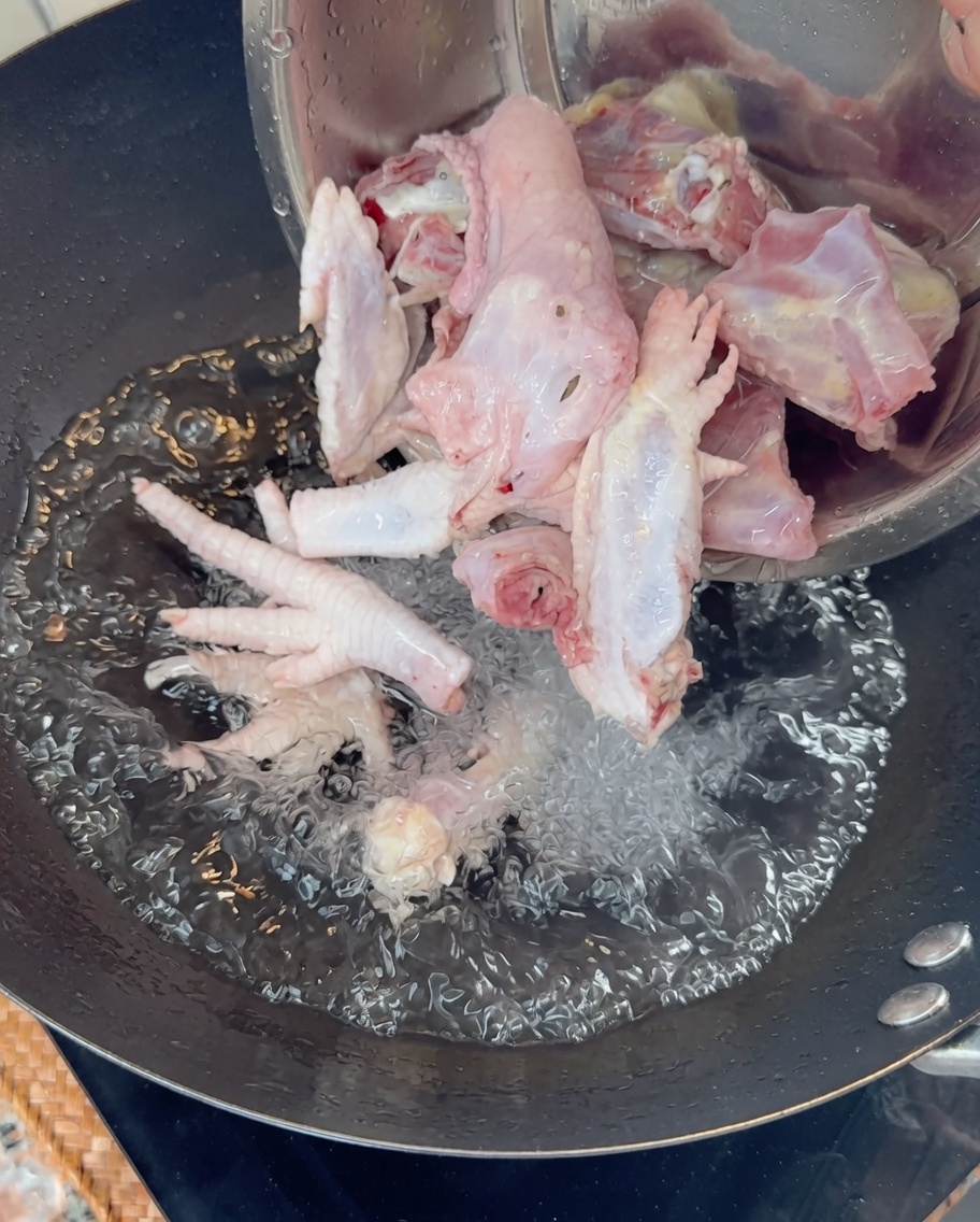 Vertiendo huesos y patas de pollo crudas en un wok con agua hirviendo.