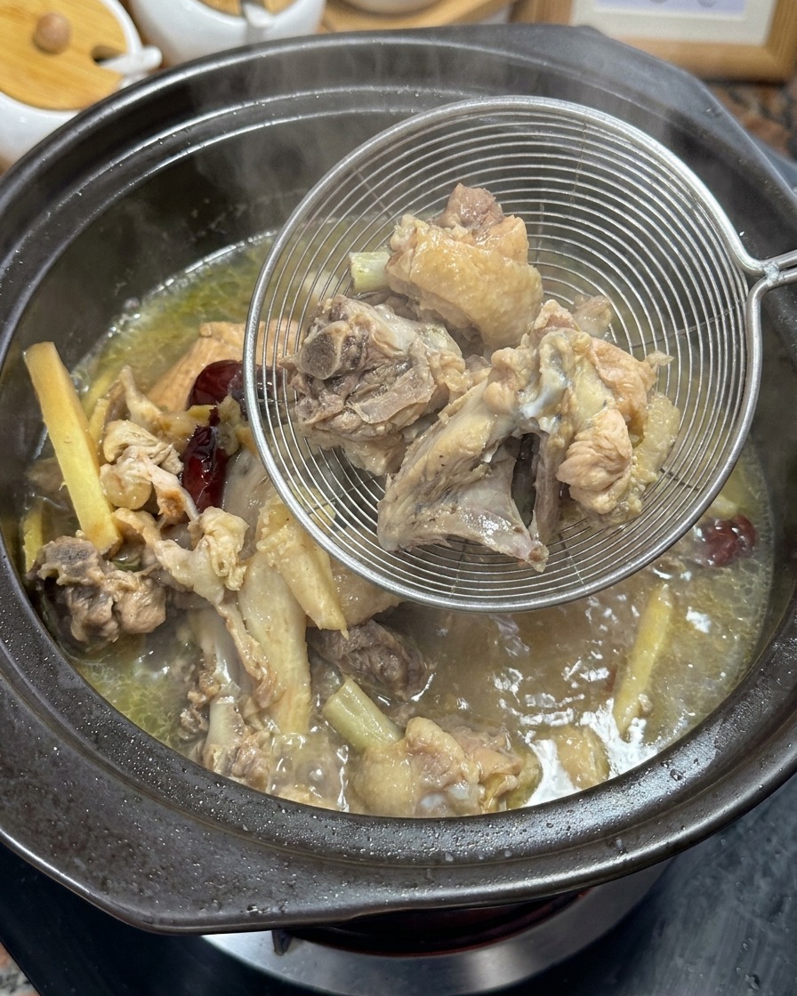 Retirando huesos de pollo cocidos y aromáticos del caldo dorado usando un colador de metal.
