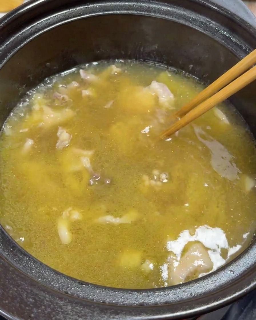 Palillos removiendo suavemente trozos de pollo y yemas en la sopa hirviendo.