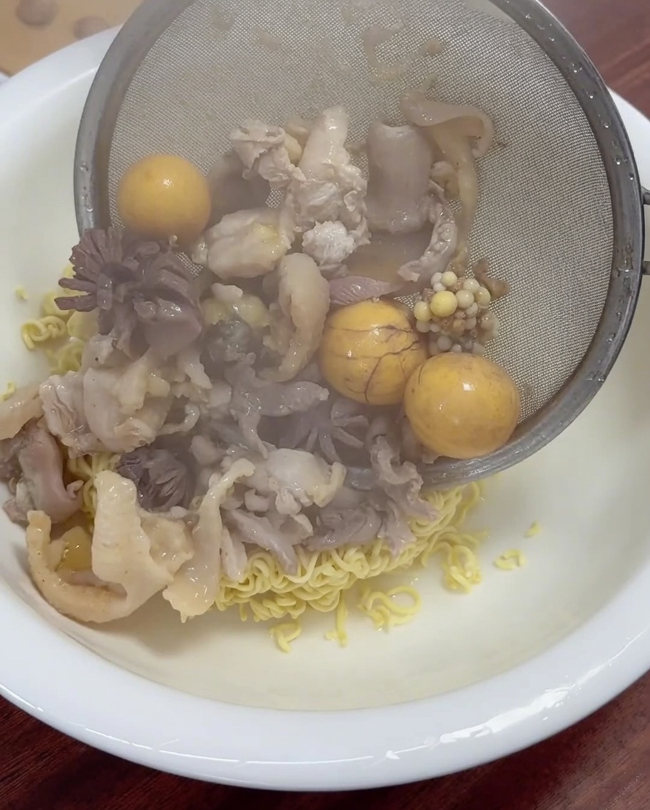 Carne de pollo y yemas recién cocidas siendo escurridas y puestas sobre un tazón de fideos.