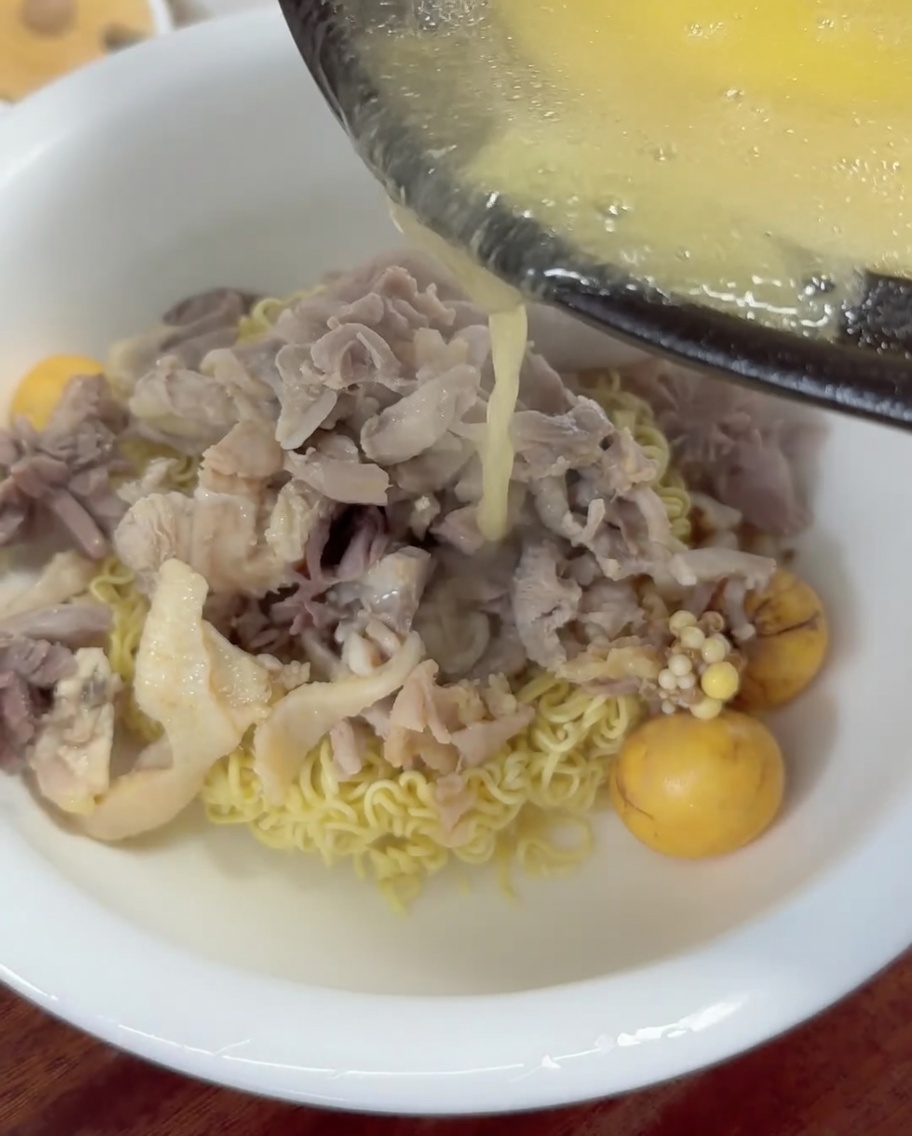 Caldo de pollo caliente y dorado vertido desde un cucharón en un tazón de fideos y pollo.