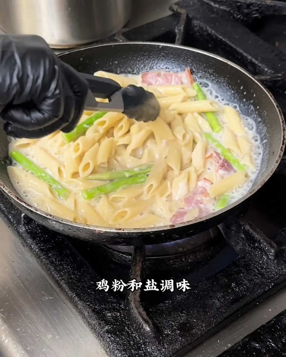 Pasta penne mezclándose con salsa blanca y trufa negra en una sartén a fuego medio.