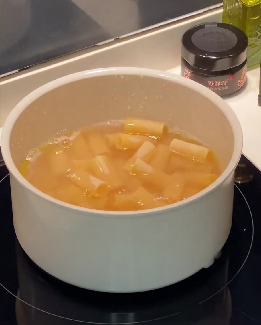 Pasta rigatoni hirviendo en una olla con agua con burbujas y gotas de aceite en la superficie.