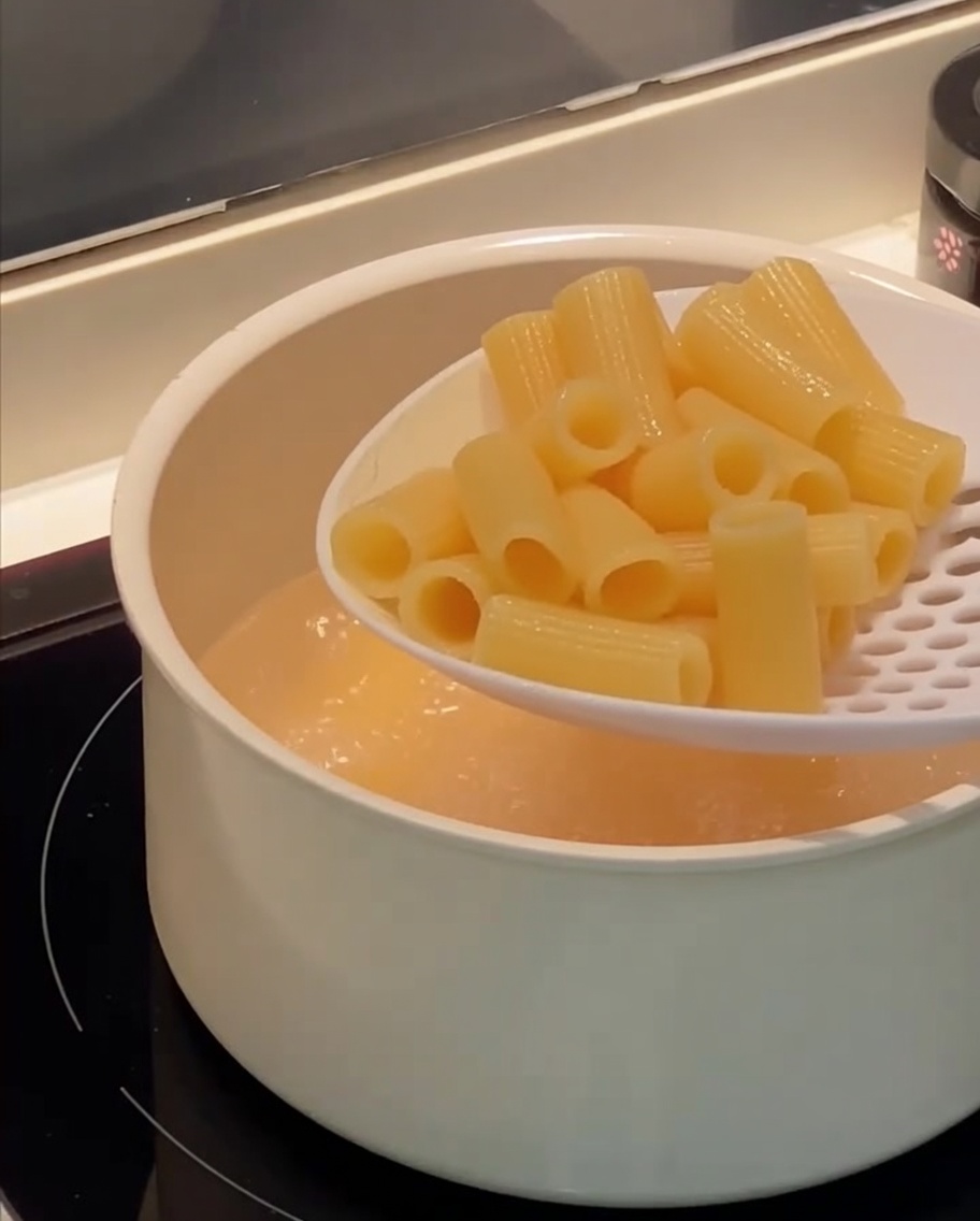 Una espumadera sacando pasta rigatoni cocida de una olla con agua hirviendo.