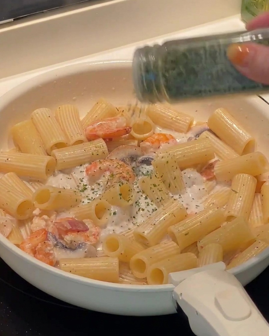 Perejil fresco picado siendo espolvoreado sobre la pasta rigatoni terminada en la sartén.