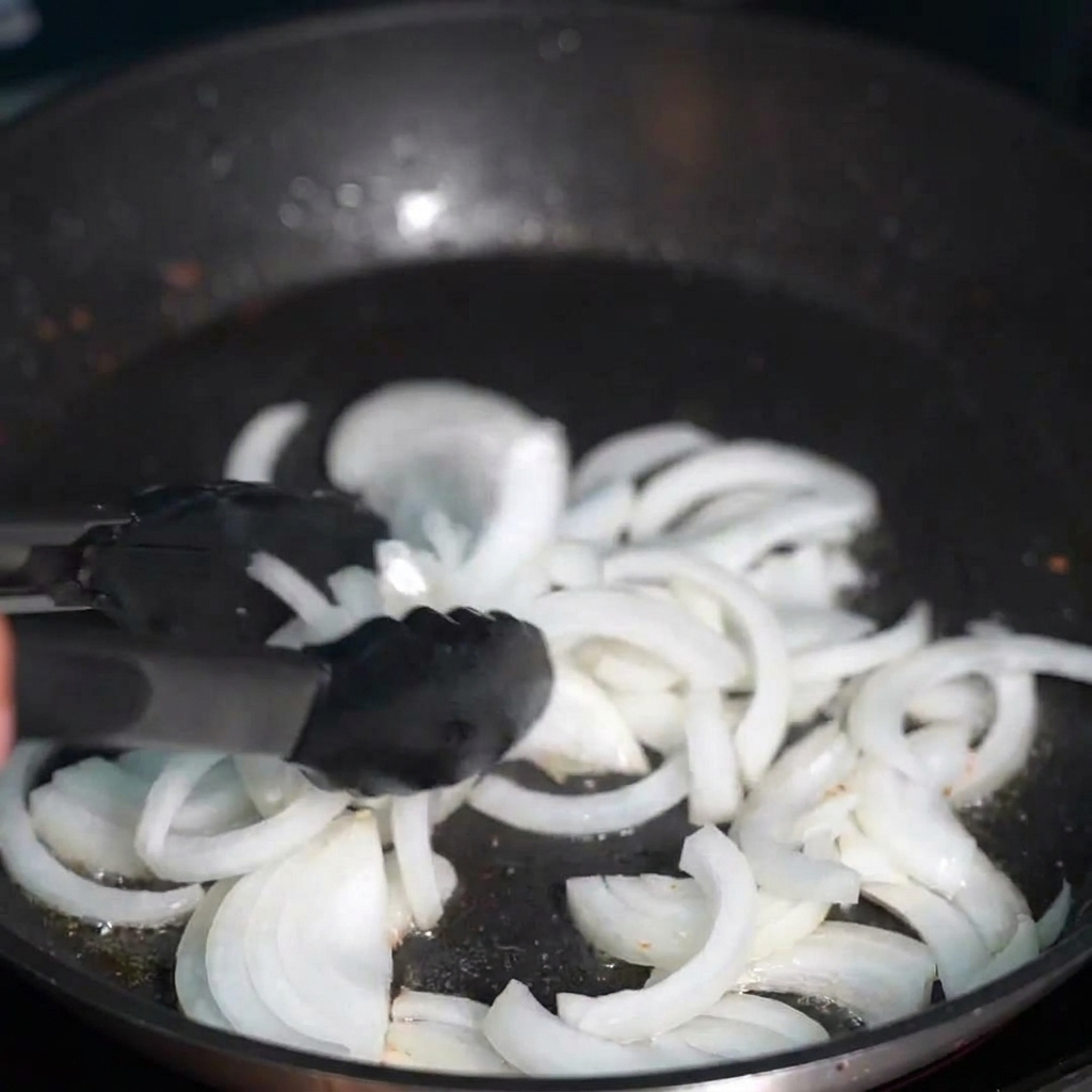 Cebollas en rodajas translúcidas salteándose en la clara y dorada grasa del tocino.