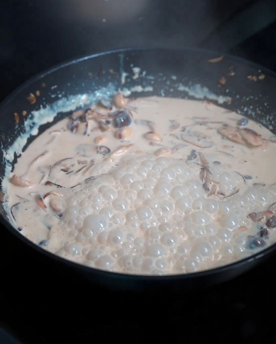 Fideos de pasta cocidos siendo incorporados a la rica salsa cremosa de setas en una sartén.