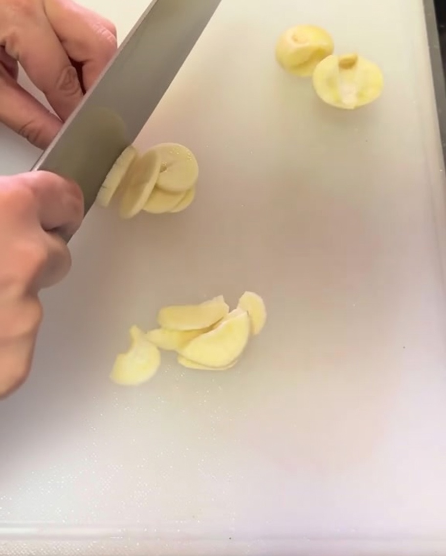 Dientes de ajo cortados finamente sobre una tabla de cortar blanca.
