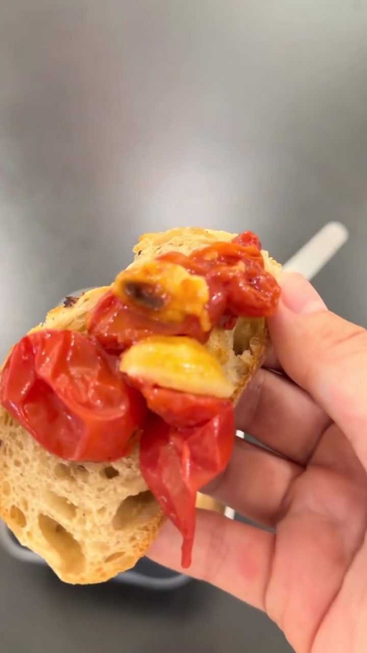 Una rebanada de pan rústico cubierta con vibrantes y brillantes tomates cherry confitados y láminas de ajo dorado.